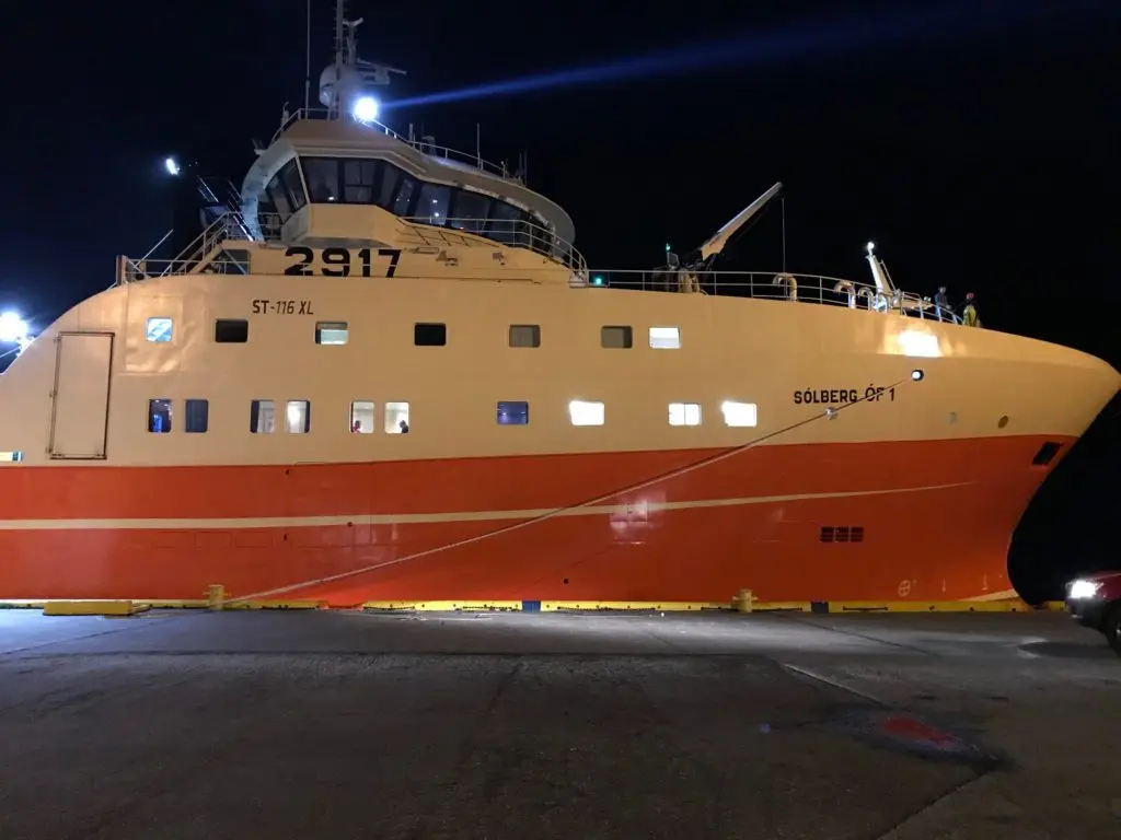 Trawler with an orange hull at the quay at night